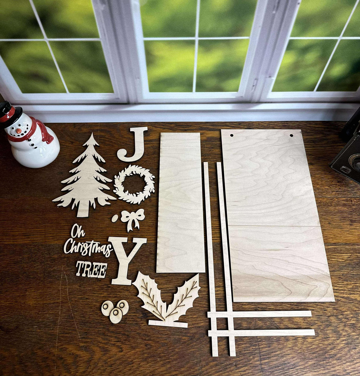 Individual laser-cut wooden layers for the JOY Christmas DIY craft kit, including wreath, letters, pine tree, holly berries and sign backers.