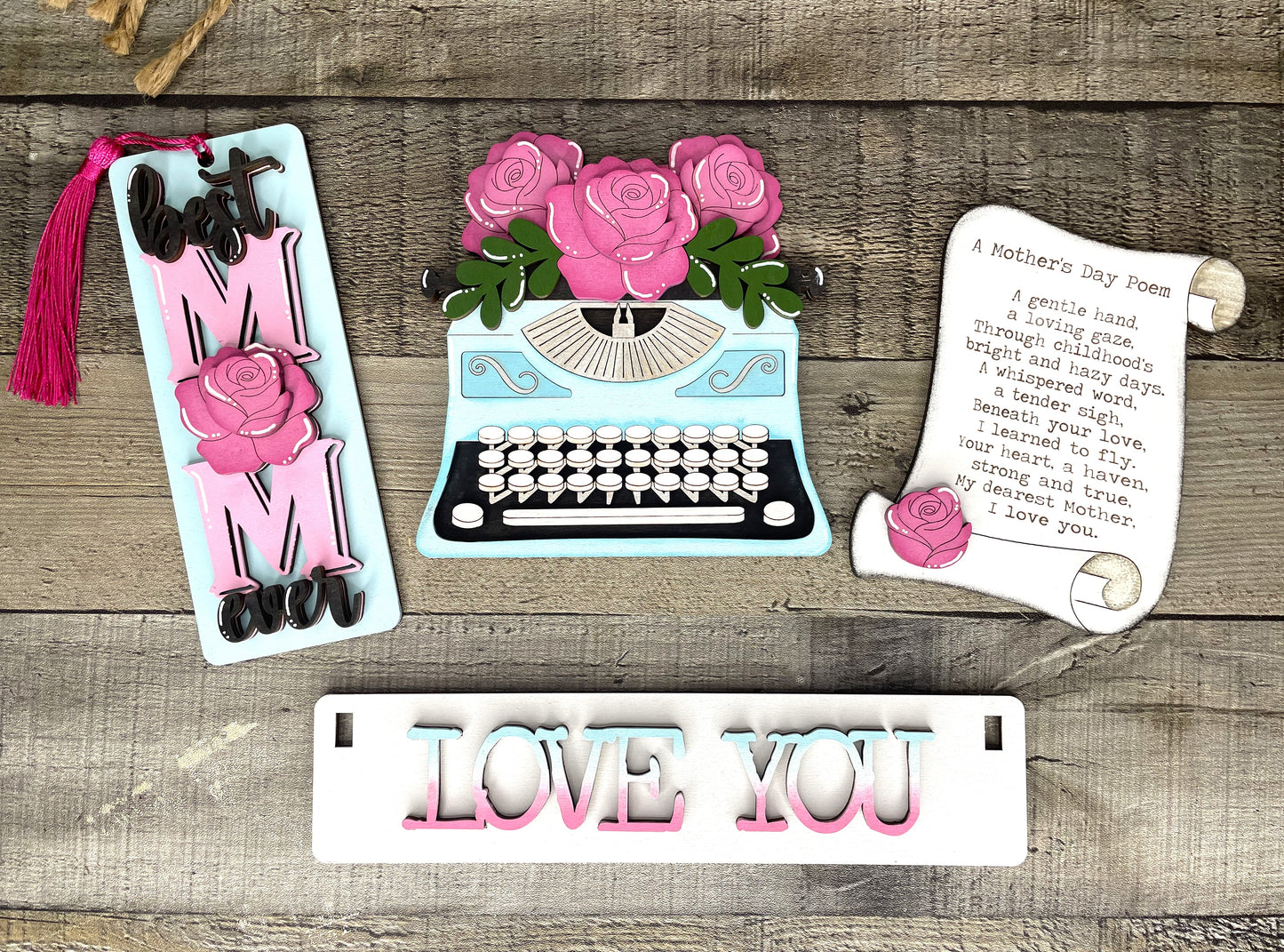 Painted inspiration version of the Laser-cut Mother's Day DIY craft kit with typewriter flower plaque, pink rose 'Best Mom Ever' bookmark, poem scroll sign, and pastel 'LOVE YOU' sign on rustic wood background - kit comes unfinished
