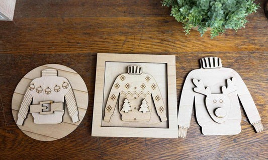 Laser-cut Christmas sweater DIY craft kits featuring Santa belt, reindeer, and tree designs on wood background — paint and assemble yourself.
