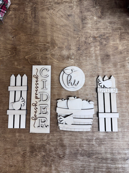 Flat lay of unfinished apple cider fall door insert kit with five decorative wooden components