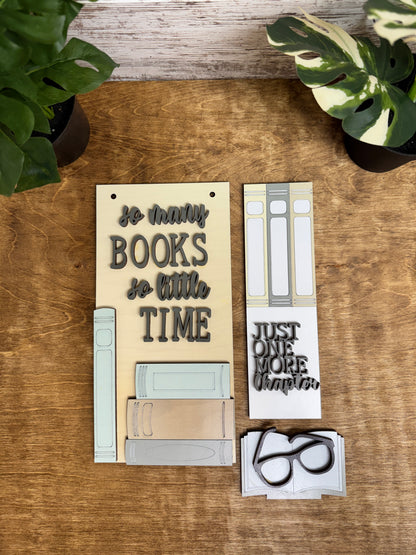Painted book lover post kit components with layered lettering, book designs and reading glasses arranged on a tabletop.