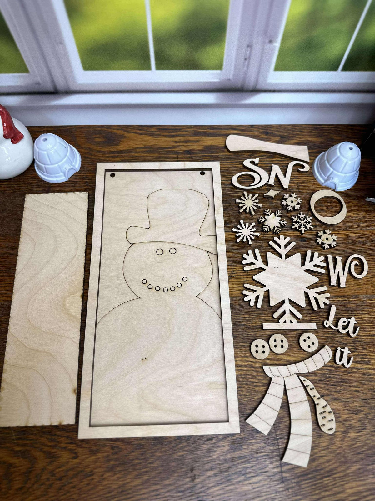 Individual unfinished laser-cut wooden pieces for the Let It Snow winter DIY craft kit, including snowman layers, lettering and snowflakes.