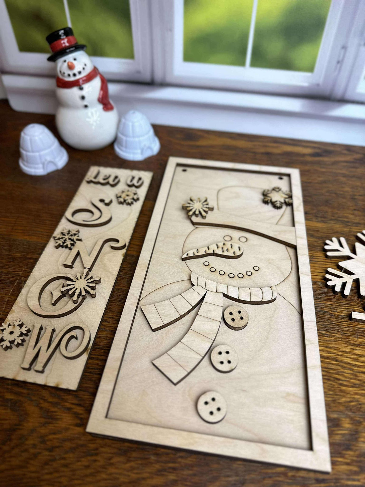 Close-up of unfinished wooden snowman hanging sign with top hat, scarf and buttons beside the Let It Snow vertical post insert.