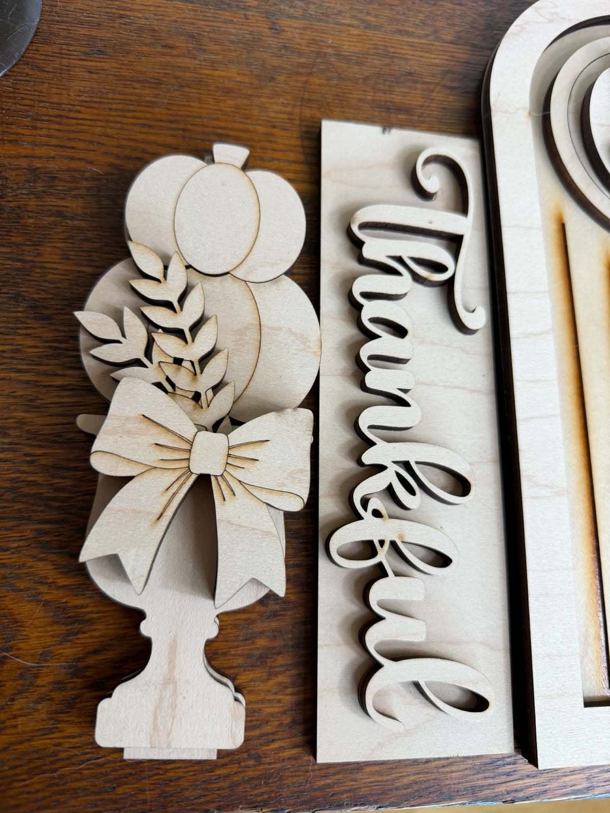 Unfinished laser-cut pumpkin topiary with bow beside layered Thankful wood sign