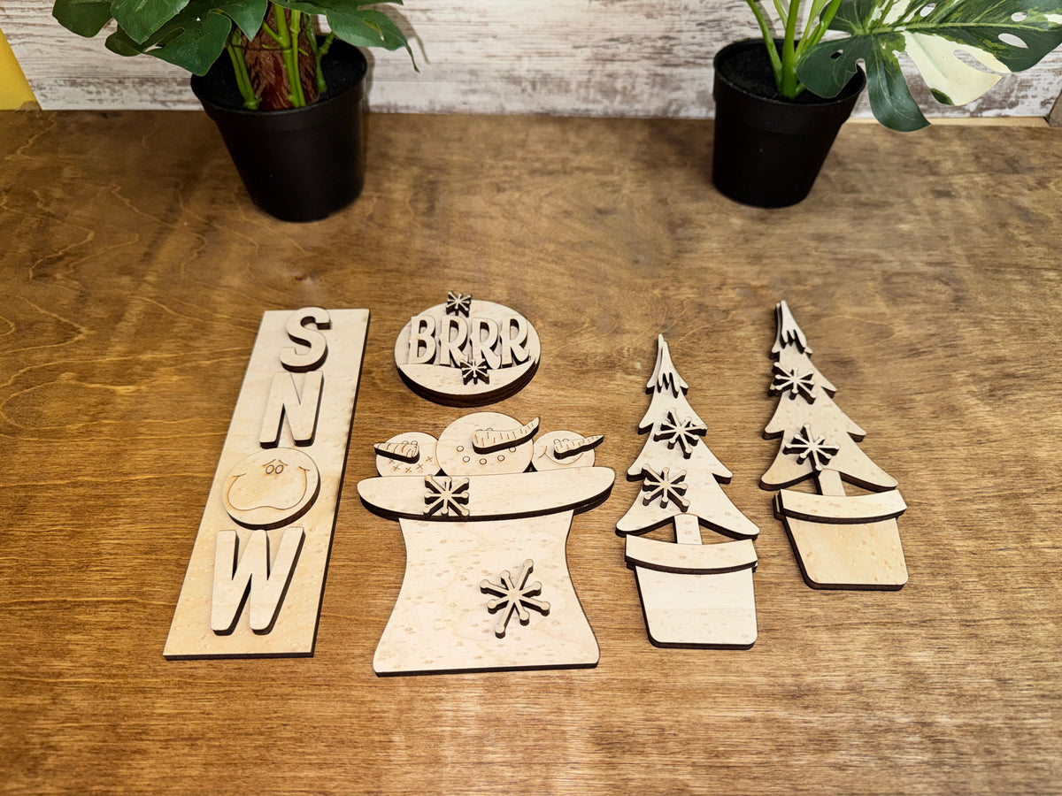 Unfinished laser-cut wood winter craft kit with layered snowmen, snowflakes and potted evergreen trees